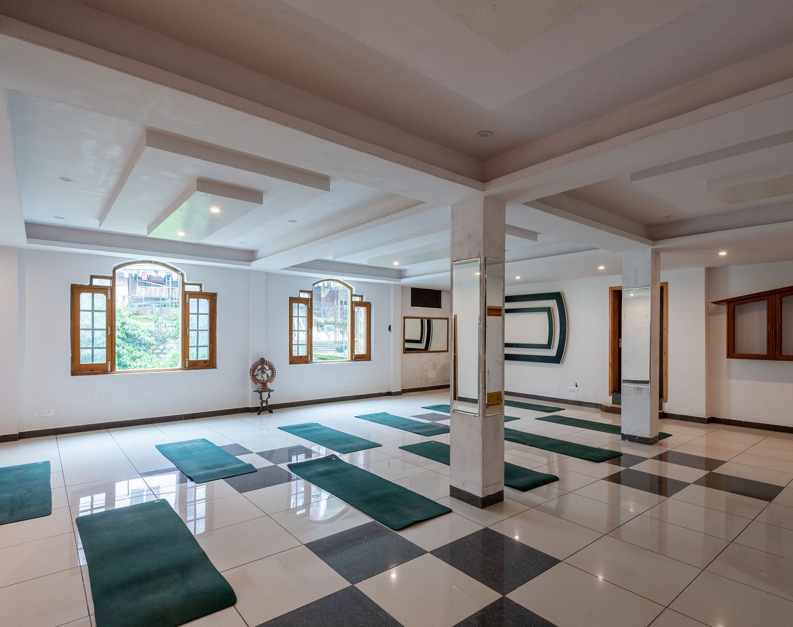 A spacious yoga studio with a tiled floor, large windows, and multiple green yoga mats laid out - DLS Meghavan Resort